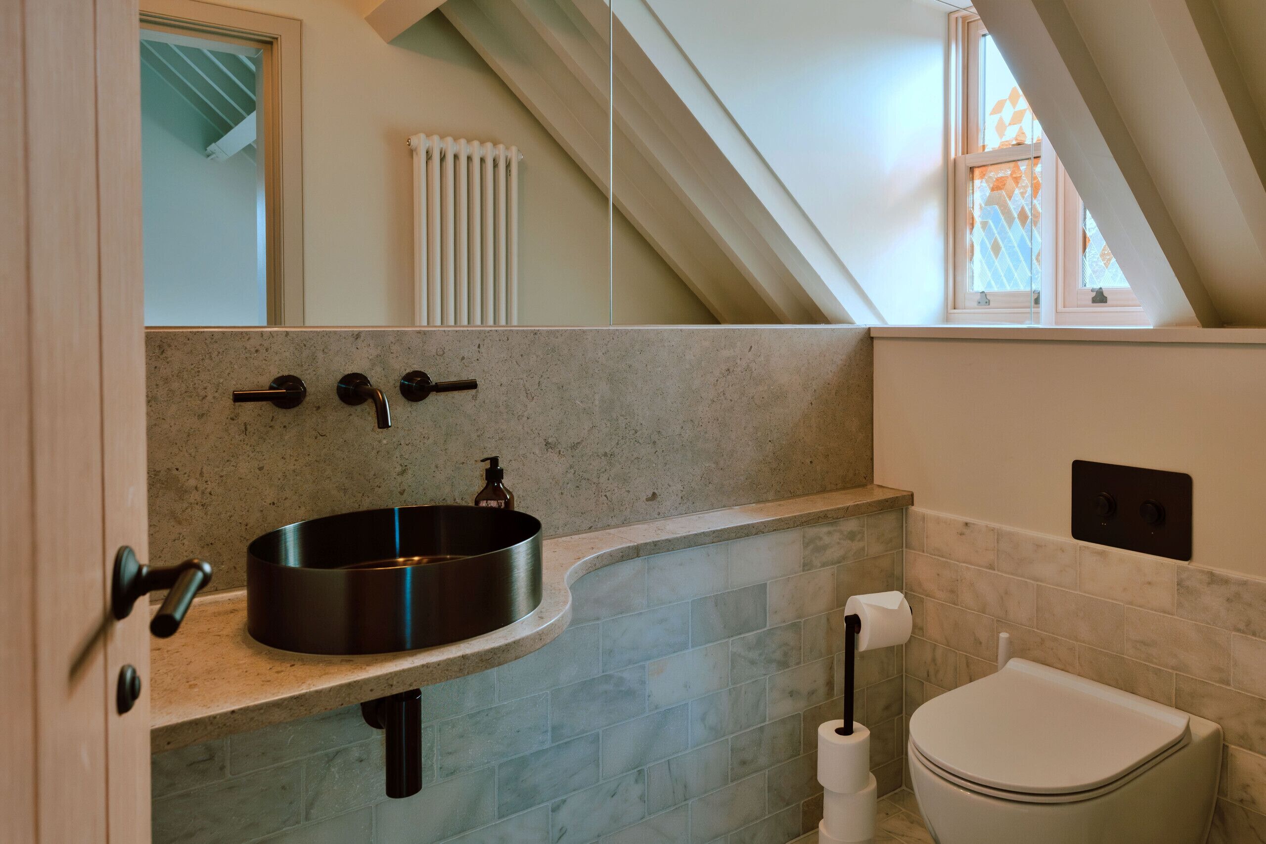 Un baño moderno con un lavamanos curvo, inodoro y radiador visible.