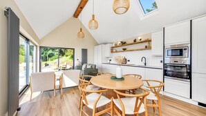 Una cocina moderna con armarios blancos, una mesa de comedor redonda y sillas de madera. Una ventana grande ofrece vistas al exterior.