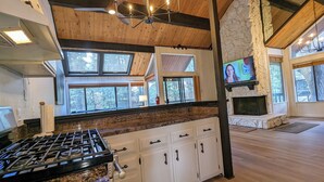 A modern kitchen with a gas stove, white cabinets, and a stone fireplace. - Snow Summit Retreat with Fireplace and Stunning Views (Big Bear Lake)