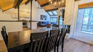A modern kitchen with white cabinets, a dining area with a wooden table and chairs, and a stone fireplace. - Snow Summit Retreat with Fireplace and Stunning Views (Big Bear Lake)