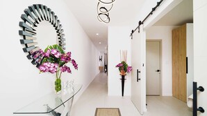 Un couloir moderne agrémenté d’une table en verre, d’un miroir noir et argenté au design original, et de deux compositions florales.