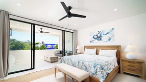 Une chambre à coucher comprenant un lit, un banc, des tables de chevet et un ventilateur de plafond.