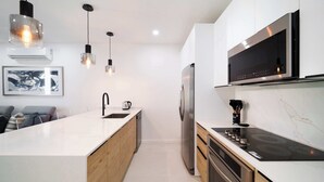 Une cuisine moderne dotée d’un îlot central, d’appareils électroménagers en acier inoxydable, de luminaires suspendus et d’un pare-feu en marbre.