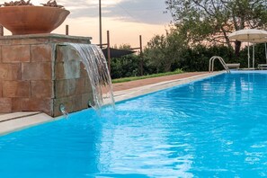 A swimming pool with a waterfall feature, surrounded by a brick wall and greenery. - Tenuta dell'Argento - Room 5 by Rentbeat  (Civitavecchia)