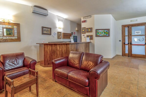 A reception area with a wooden desk, two leather sofas, and a tiled floor. - Tenuta dell'Argento - Room 5 by Rentbeat (Civitavecchia)
