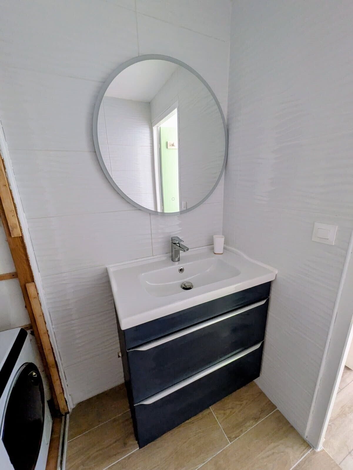 Ein Badezimmer mit einem weißen Waschtisch, einem runden Spiegel und einem Waschbecken.