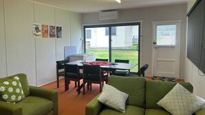 Une pièce comprenant une table à manger, des chaises, un canapé vert et une fenêtre donnant sur une maison.