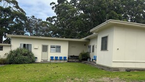 Un bâtiment d’un seul étage, doté d’un toit plat, d’un porche avec des chaises bleues et d’un petit jardin.