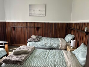 Huoneessa on kaksi sänkyä, puinen seinäpaneeli, kehystetty taulu ja yöpöytä, jossa on lamppu.