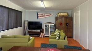 Ein Wohnzimmer mit grünen Sofas, einem Flachbildfernseher, einem Schrank mit Hüten und einem Schild mit der Aufschrift 'Welcome to Bemm River Bungalows'.