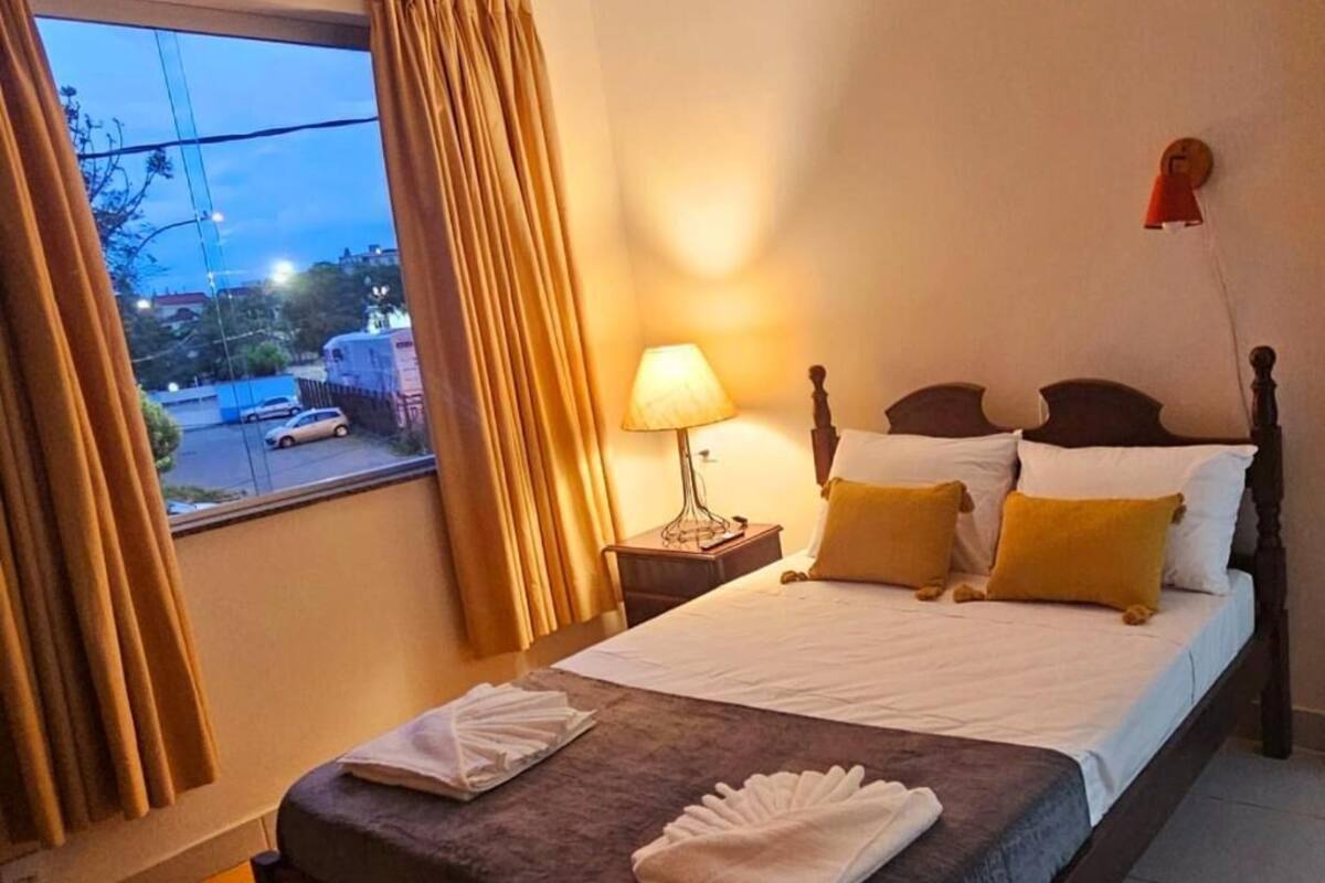 A hotel room with a bed, a nightstand, a lamp, and a window with curtains.