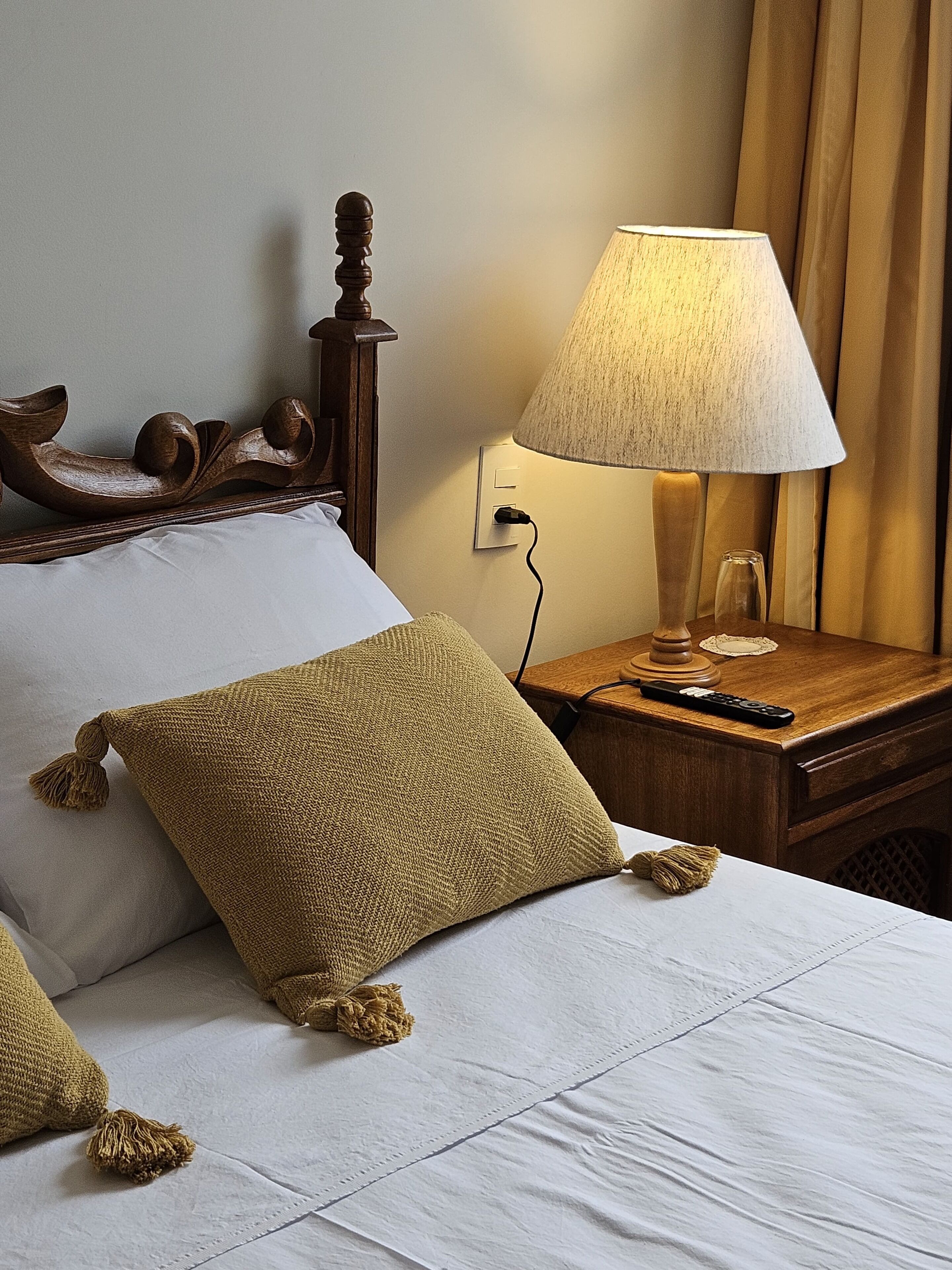 Un lit bien fait, avec une tête de lit en bois, une lampe sur une table de chevet et une télécommande sur la table.