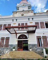 Un edificio histórico con una torre de reloj, un acceso cubierto y una escalera que conduce a la entrada principal.