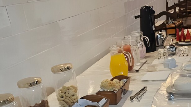 A breakfast buffet with various pastries, cakes, and beverages on a marble table. - Hotel Barbacena (Barbacena)