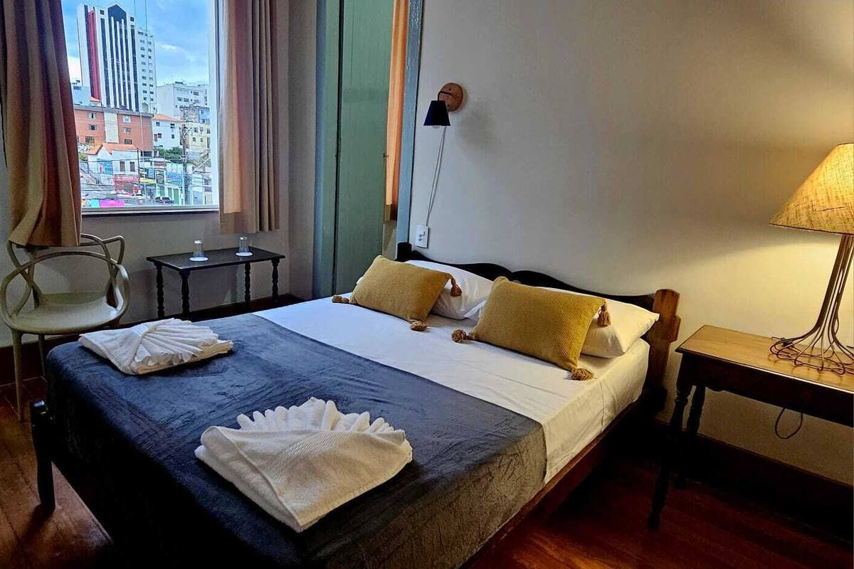 A hotel room with a bed, a chair, a table, and a lamp.