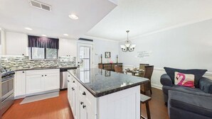 A modern kitchen with white cabinets, a granite countertop, and a dining area with a chandelier.