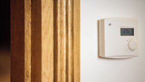 A thermostat on a wall displaying a temperature of 26 degrees.