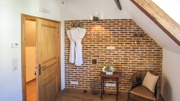 A room with a wooden door, a brick wall, a small table with a vase, and a leather chair.