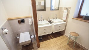A bathroom with two sinks, a toilet, and a small stool.