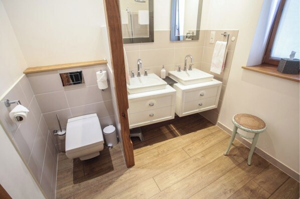 Un baño con dos lavamanos, un inodoro y un taburete pequeño.
