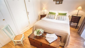 A bedroom with a large bed, two bedside tables, a wooden chest, a chair, and a small table with a flower arrangement.