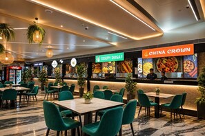 A restaurant with green chairs and tables, a Coca-Cola fridge, and signs for 'GUDUPI DOSAI' and 'CHINA CROWN'.