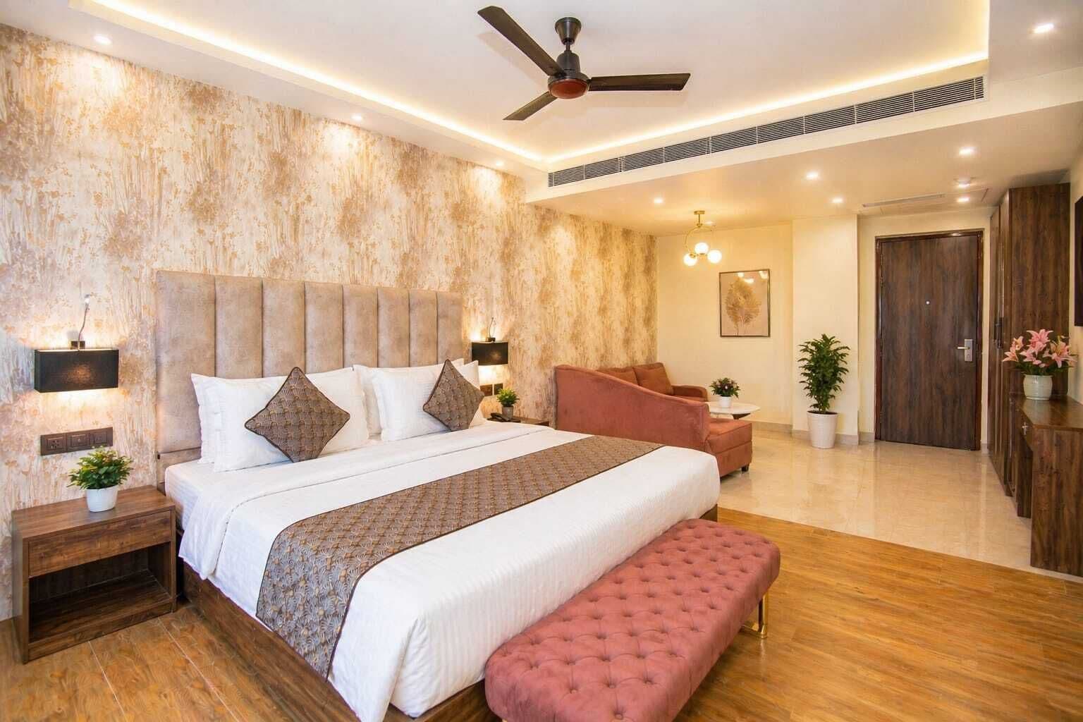 A bedroom with a large bed, a ceiling fan, a nightstand, a bench, a sofa, and a door.