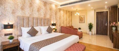 A bedroom with a large bed, a ceiling fan, a nightstand, a bench, a sofa, and a door.