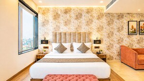 A modern hotel room with a large bed, a pink ottoman, a city view, and a patterned wall. - Hotel Avadh Classio (Faizabad)