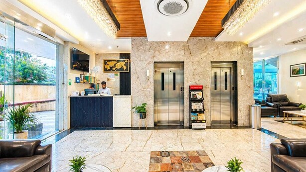 A modern hotel lobby with a reception desk, two elevators, leather seating, marble flooring, and potted plants. - Hotel Avadh Classio (Faizabad)