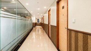 A long, well-lit hallway with glass walls on one side and wooden doors on the other. - Hotel Avadh Classio (Faizabad)