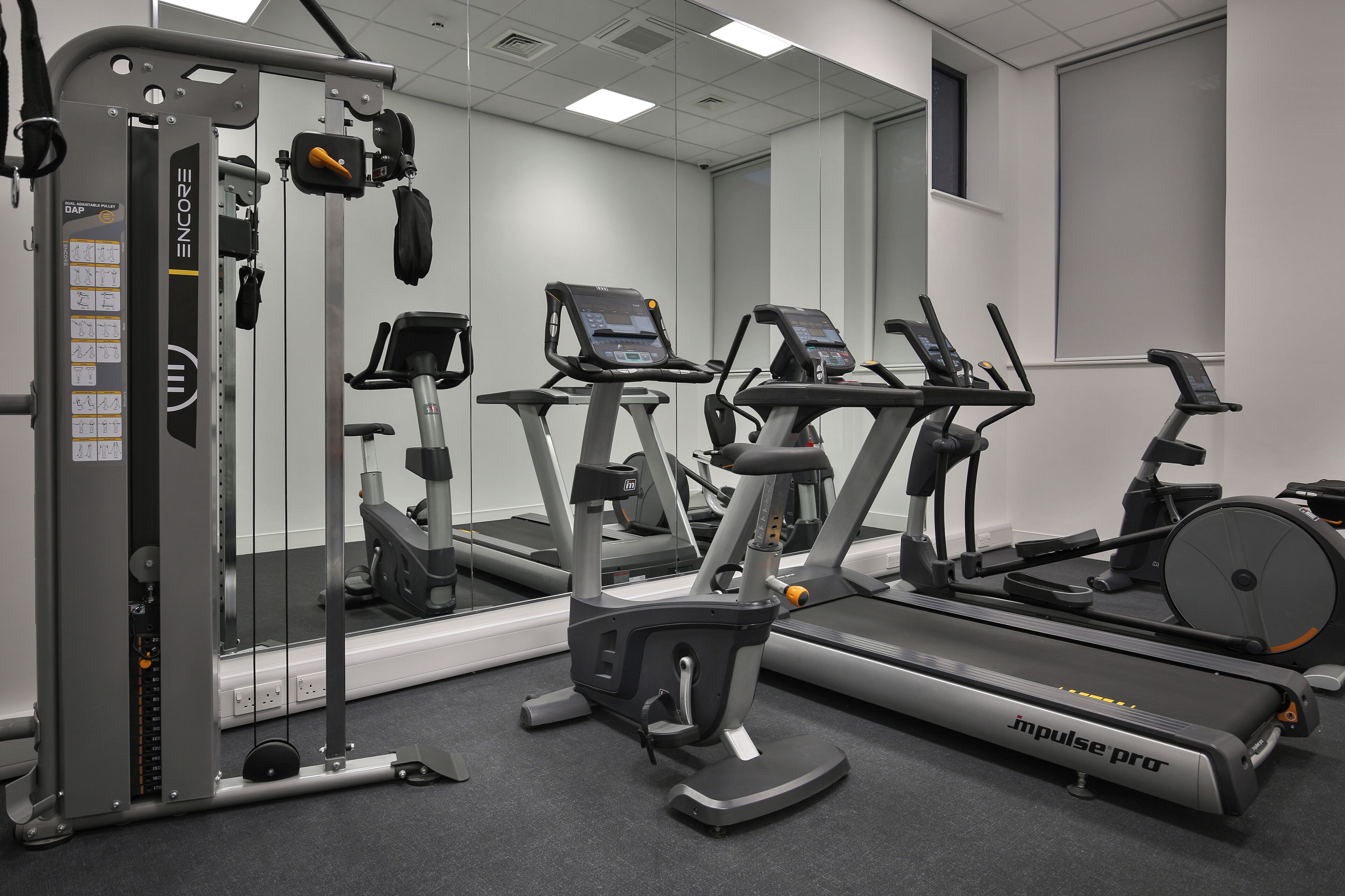 Une salle de sport équipée de divers appareils d’exercice, notamment un tapis de course, un vélo elliptique et des appareils de musculation.