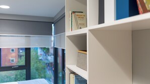 Een boekenplank met boeken en een ladder, een raam met uitzicht op gebouwen, en een witte muur.