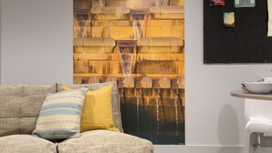 Een woonkamer met een bank, een salontafel en een wanddecoratie met een waterval.