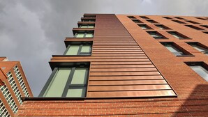 Een hoog gebouw met een modern ontwerp, met een combinatie van baksteen en metalen panelen, grote ramen en een schuin dak.