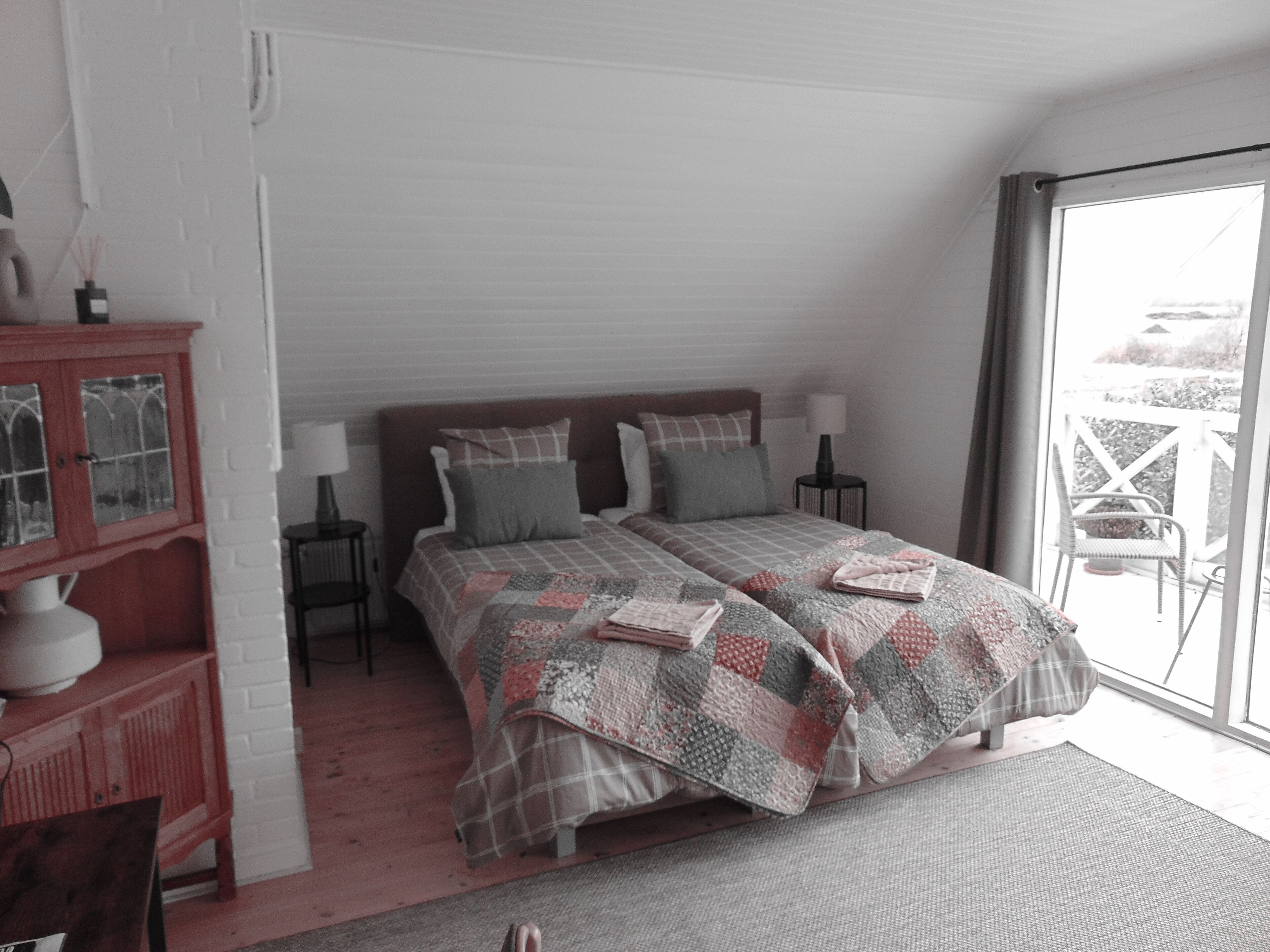 A bedroom with a large bed, two bedside tables, a nightstand, a wooden cabinet, and a view through a glass door.