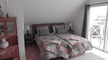 A bedroom with a large bed, two bedside tables, a nightstand, a wooden cabinet, and a view through a glass door.