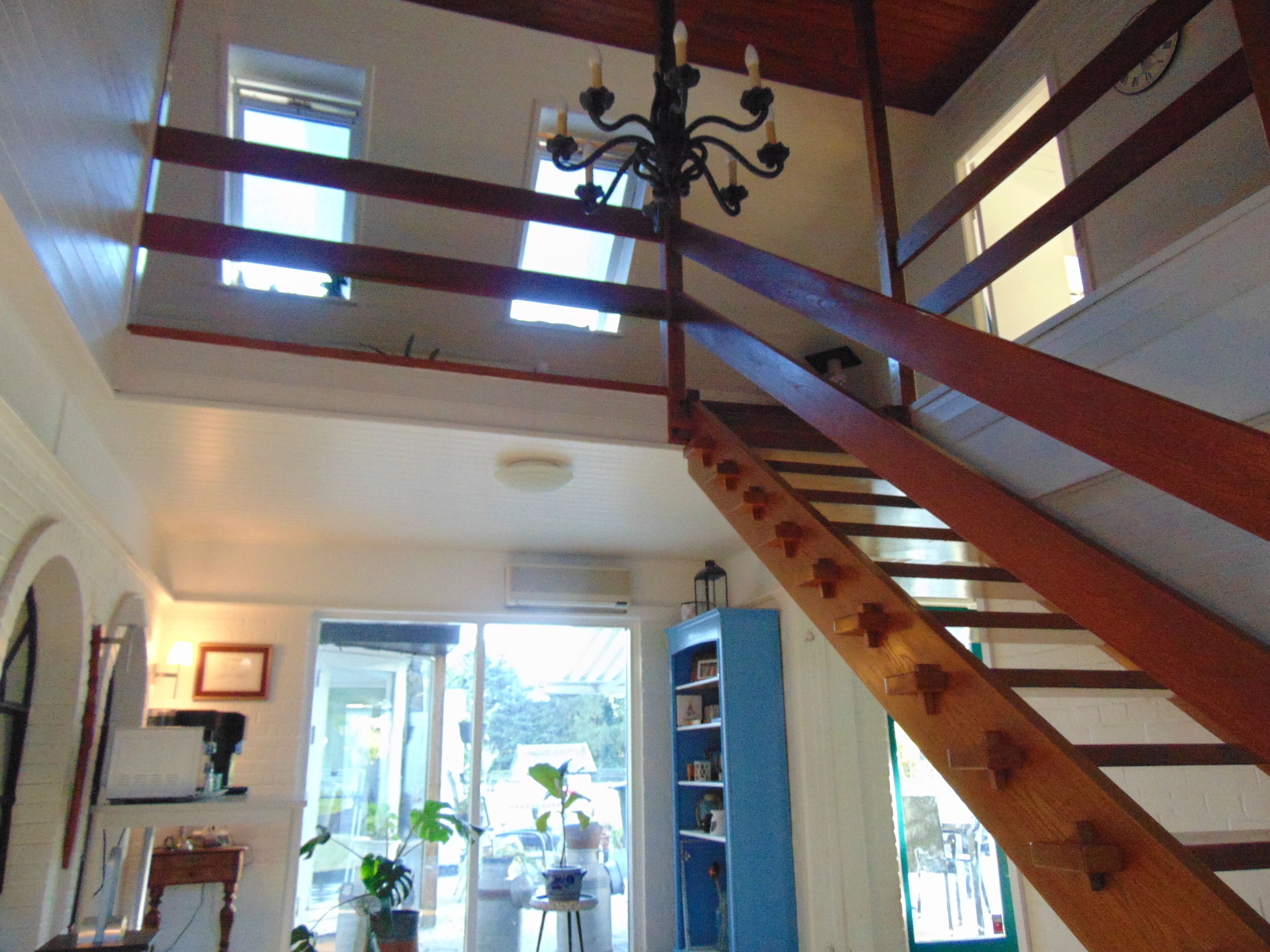 A staircase with wooden railings and a chandelier. There is a bookshelf and a small table with plants.