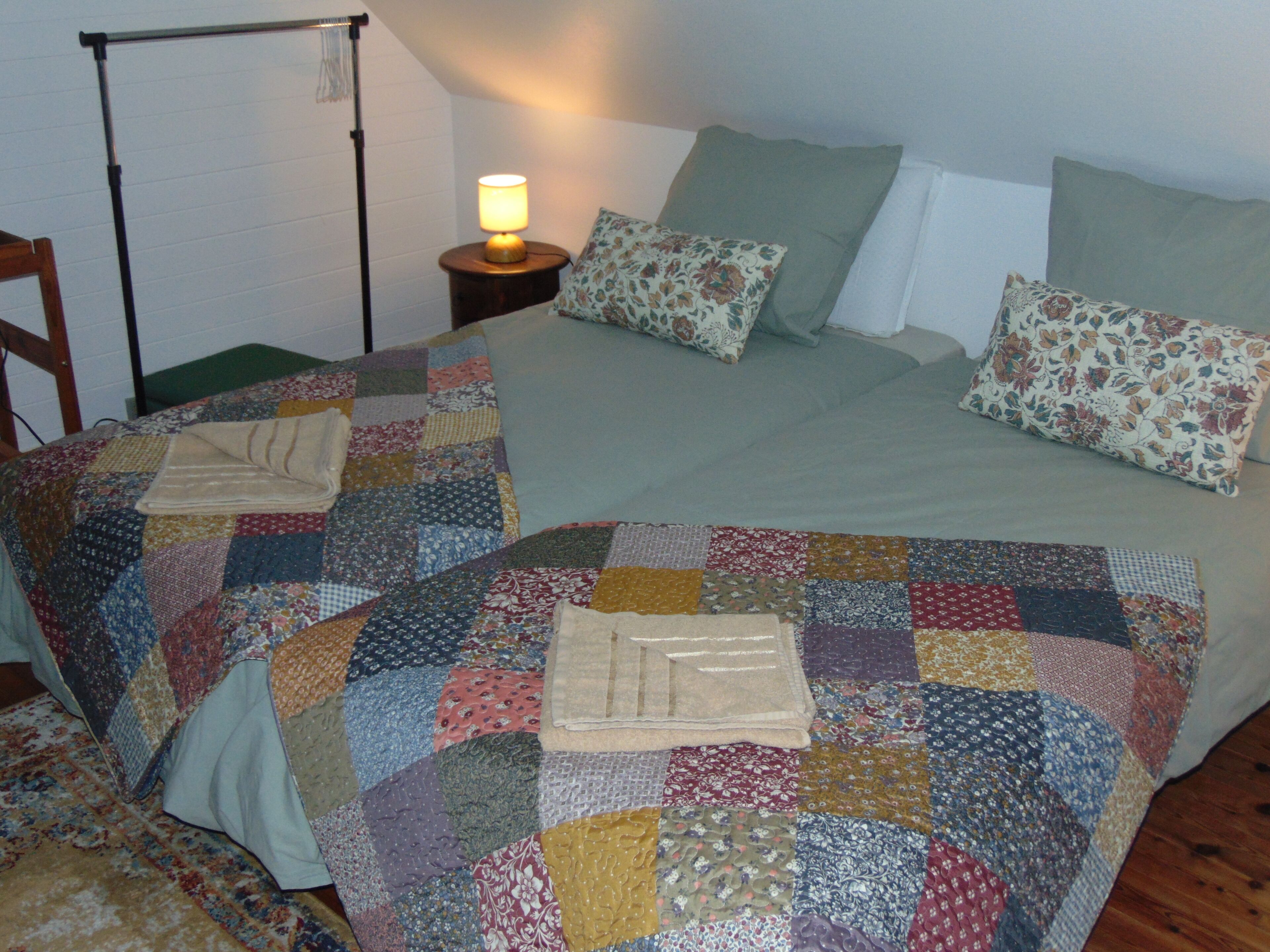 A bed with a patchwork quilt, two pillows, a bedside lamp, and a wooden chair.