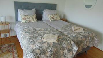 Uma cama de casal com colcha acolchoada, duas almofadas, uma mesinha de cabeceira e um espelho na parede.