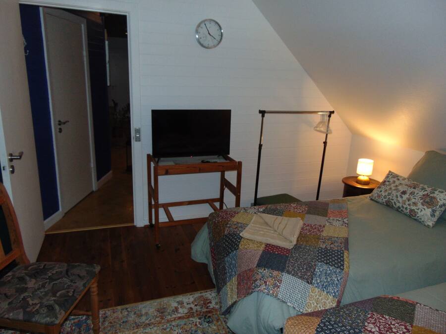 Een slaapkamer met een bed, een stoel, een televisie, een lamp en een klok aan de muur.