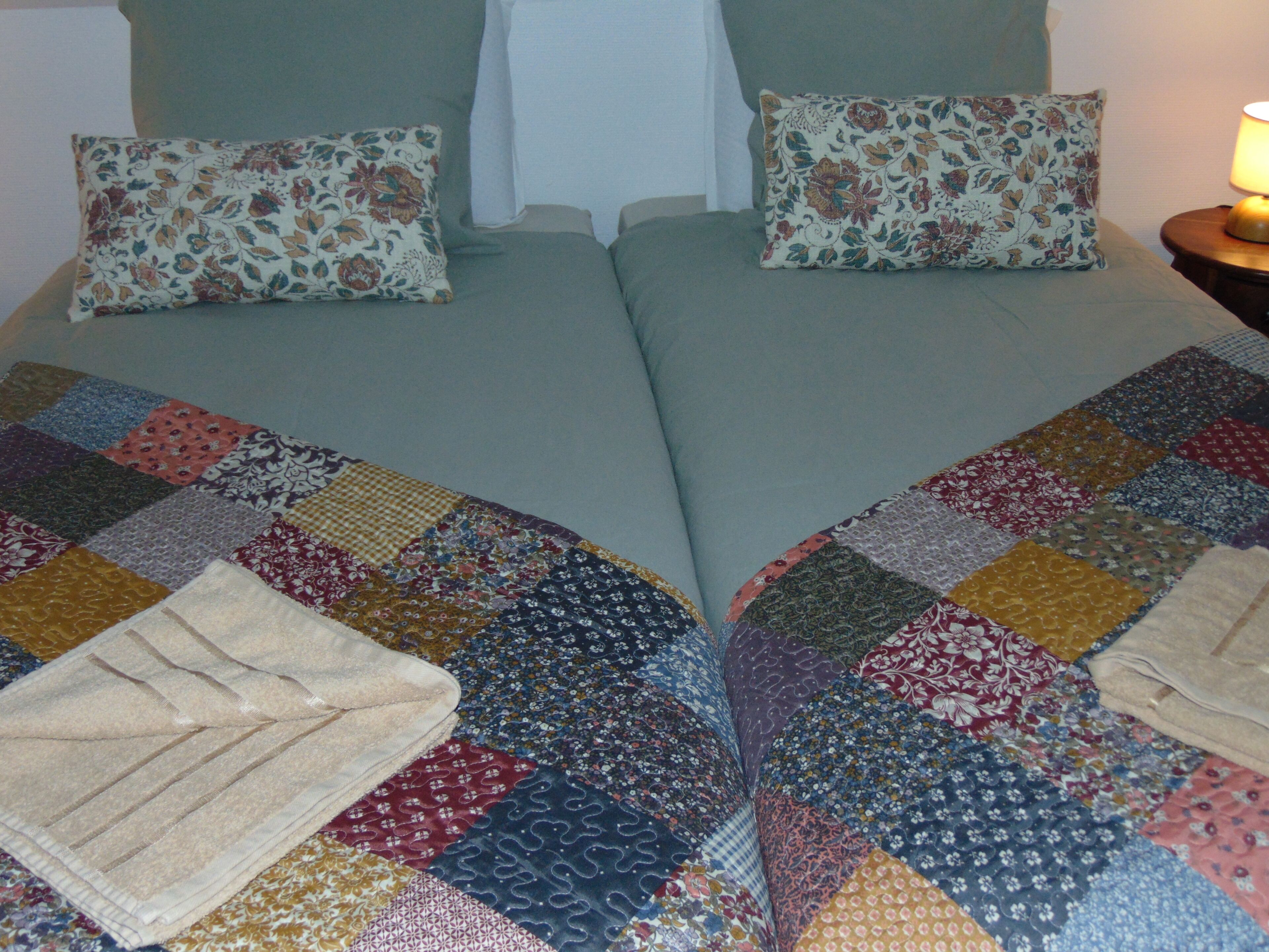 A bed with a colorful patchwork quilt and two floral pillows.