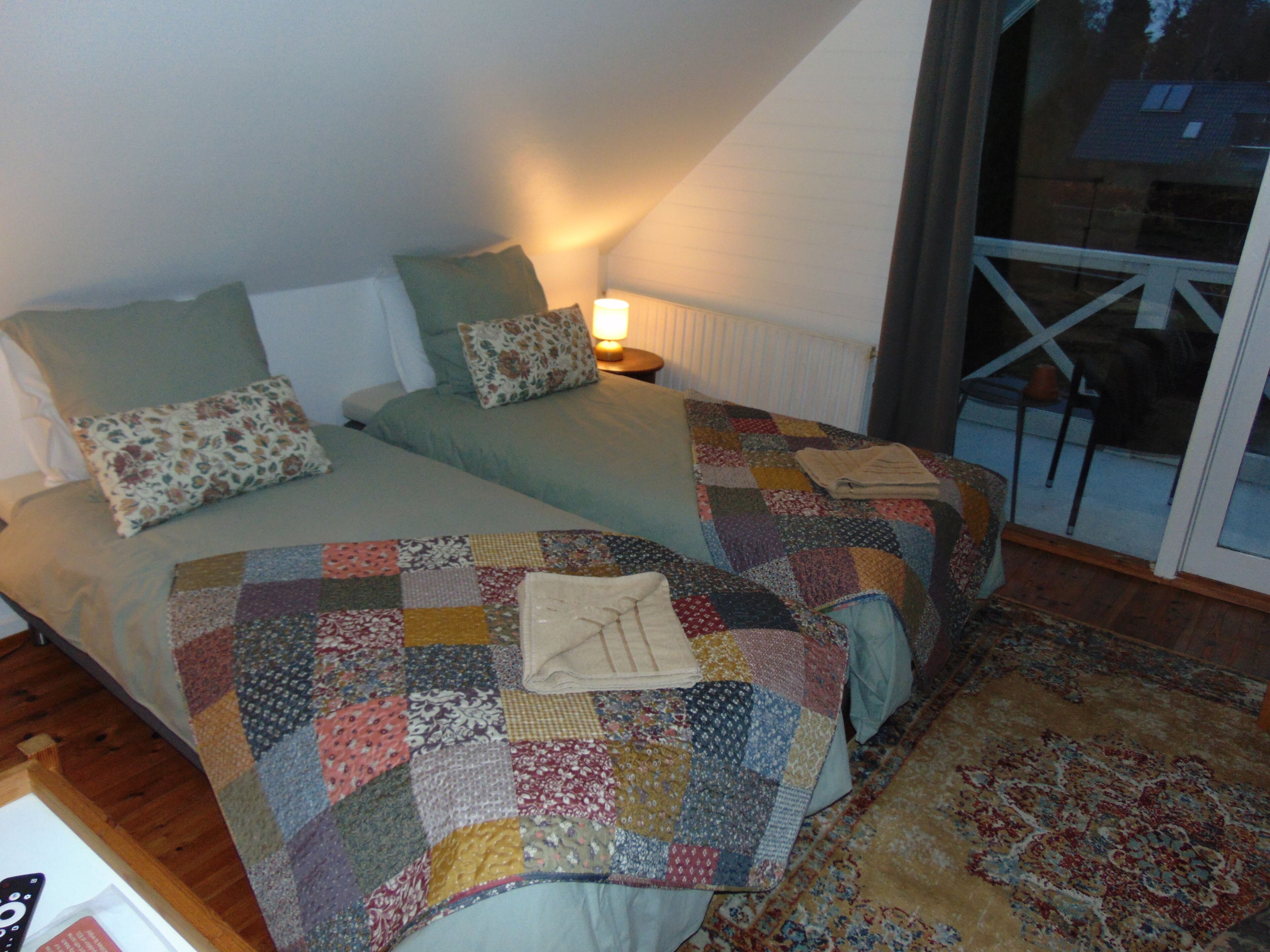 Un dormitorio con dos camas, una colcha estampada y una mesita de noche con una lámpara.