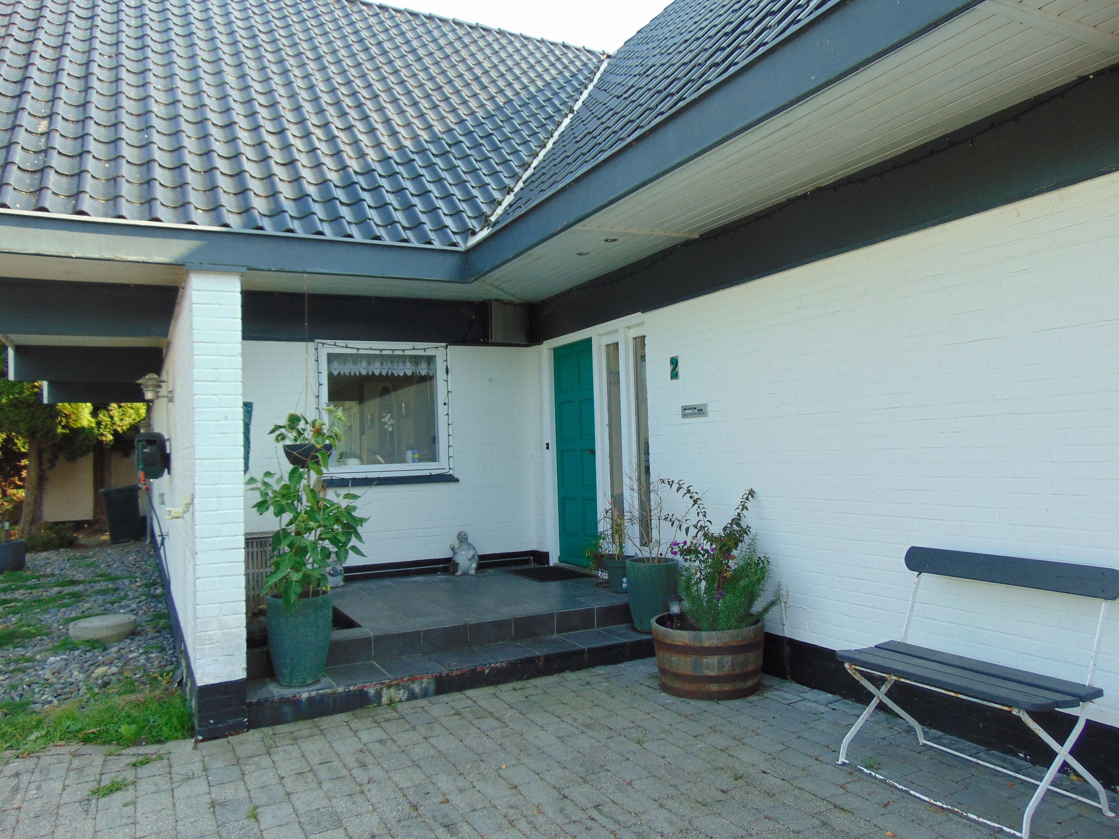 A house with a tiled roof, a white exterior, a green door, and a bench outside.