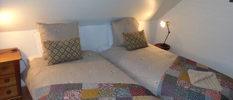 A bedroom with two beds, a wooden nightstand, a lamp, and a quilt on the floor.