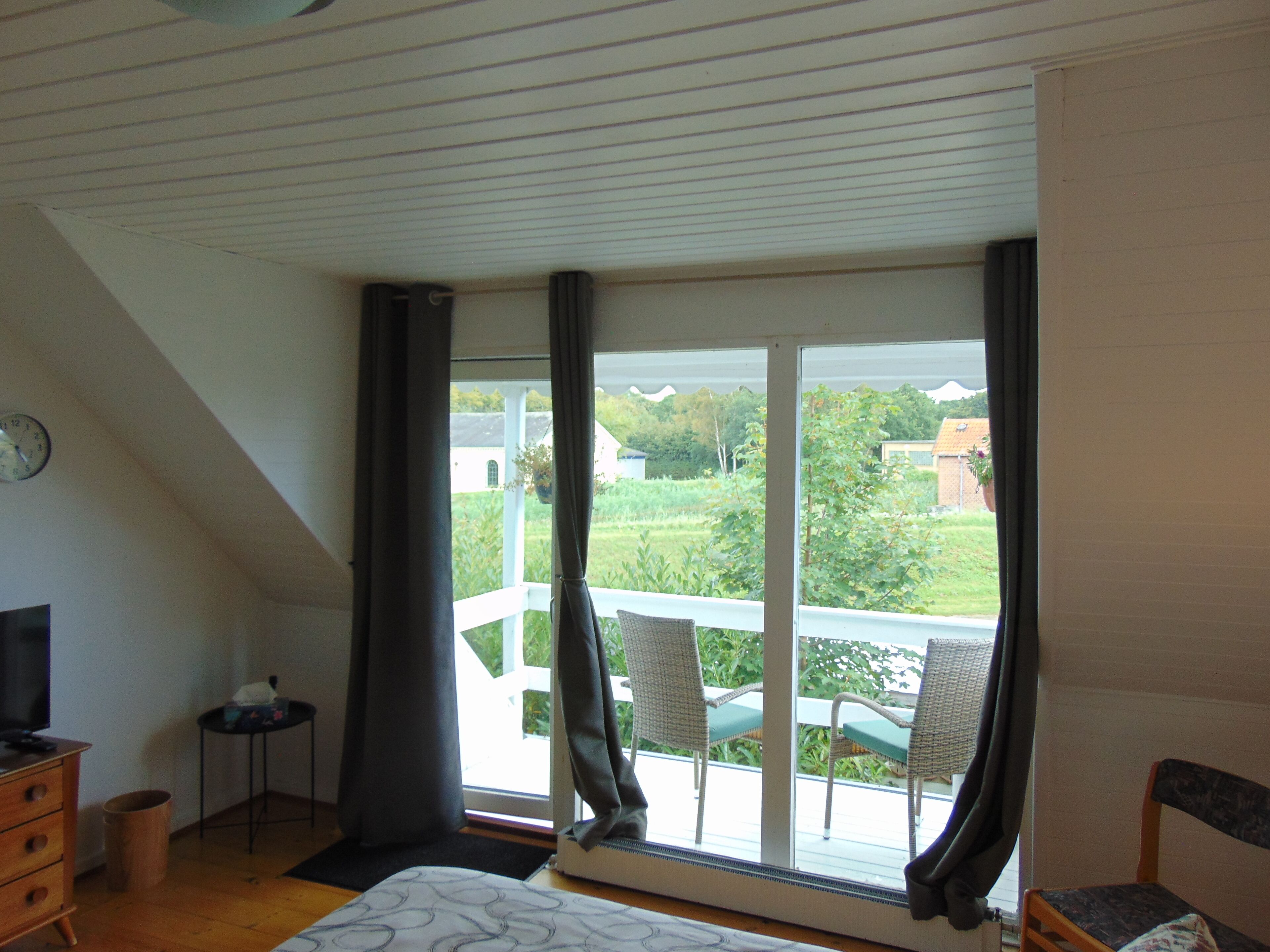 A bedroom with a large window, a bed, a dresser, a television, and a small table.