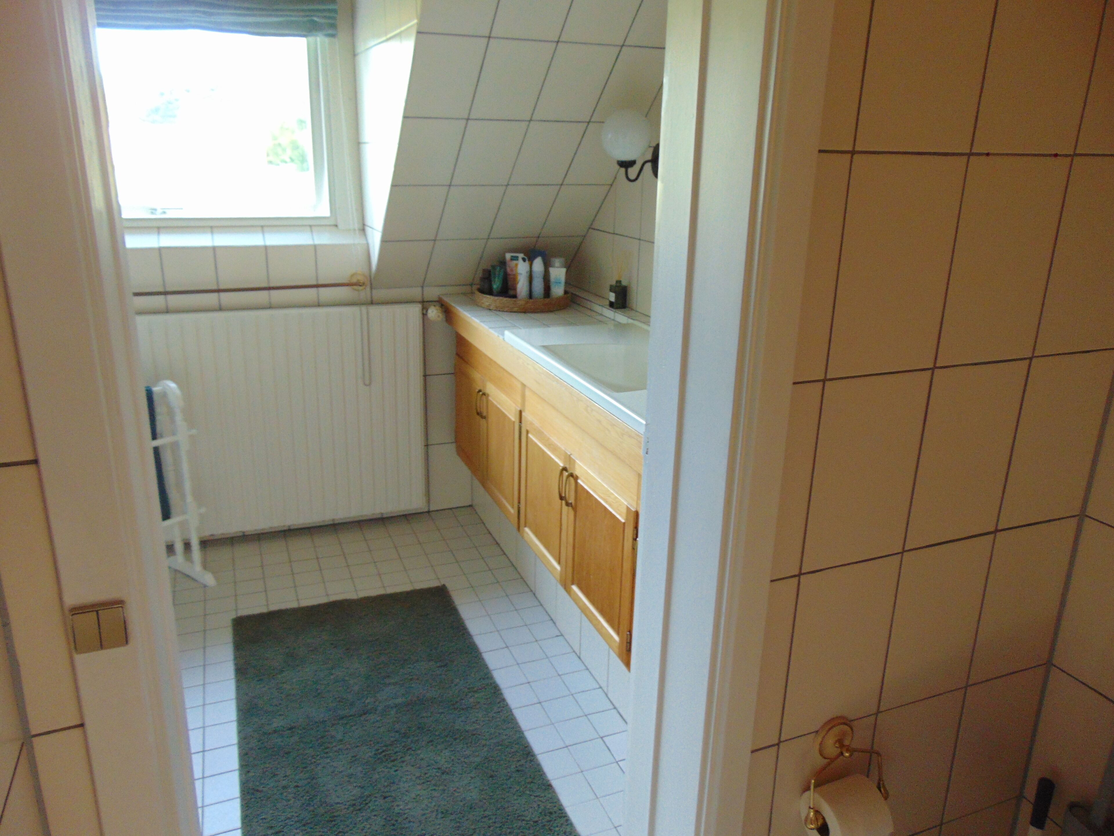 A small, narrow bathroom with a window, a radiator, a sink, and a toilet.