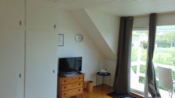 Un dormitorio con un aparador de madera, un televisor, una mesita y una ventana con cortinas.