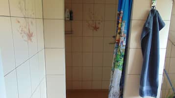 A bathroom with a shower, tiled walls, a hanging towel, and a potted plant.