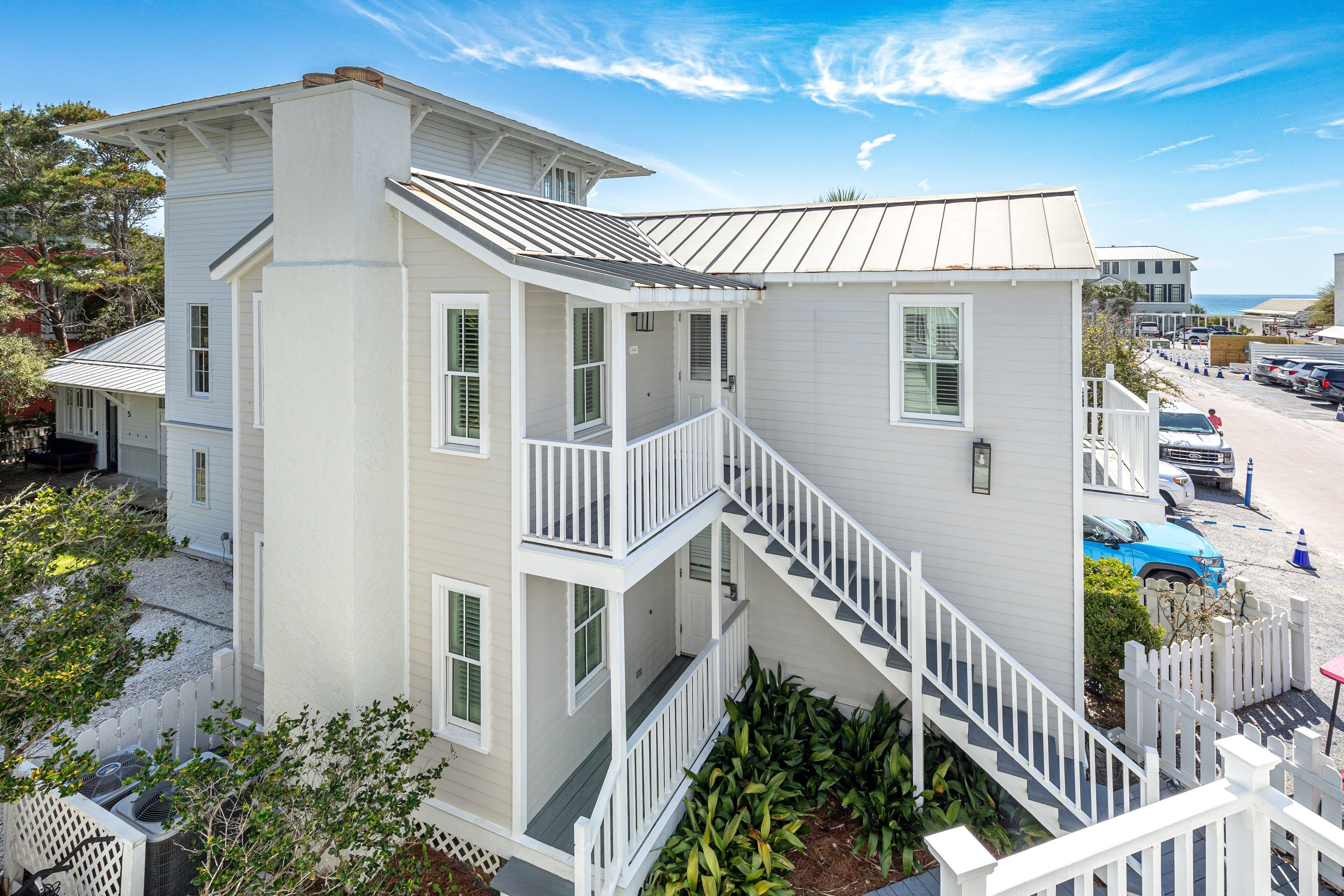 A multi-story white building with a central staircase, a covered porch, and a view of the beach.